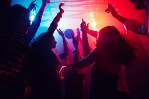 A crowd of people in silhouette dancing with hands raised up.